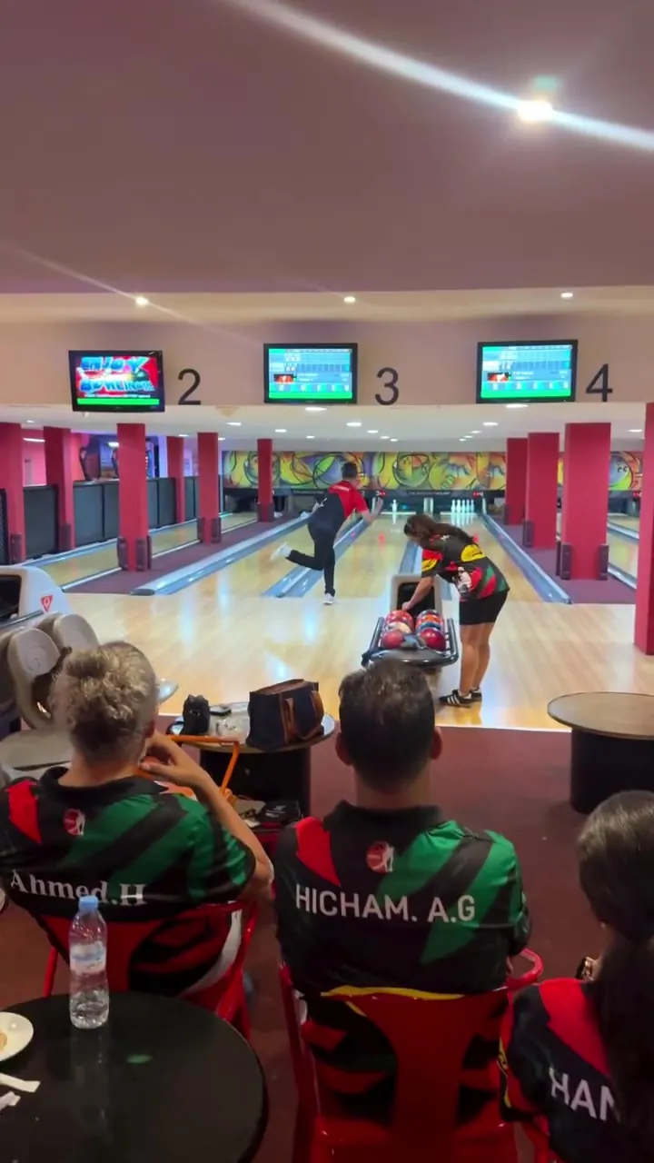Des joueurs en maillot vert et rouge assis derrière les pistes 2 à 4 pendant la compétition