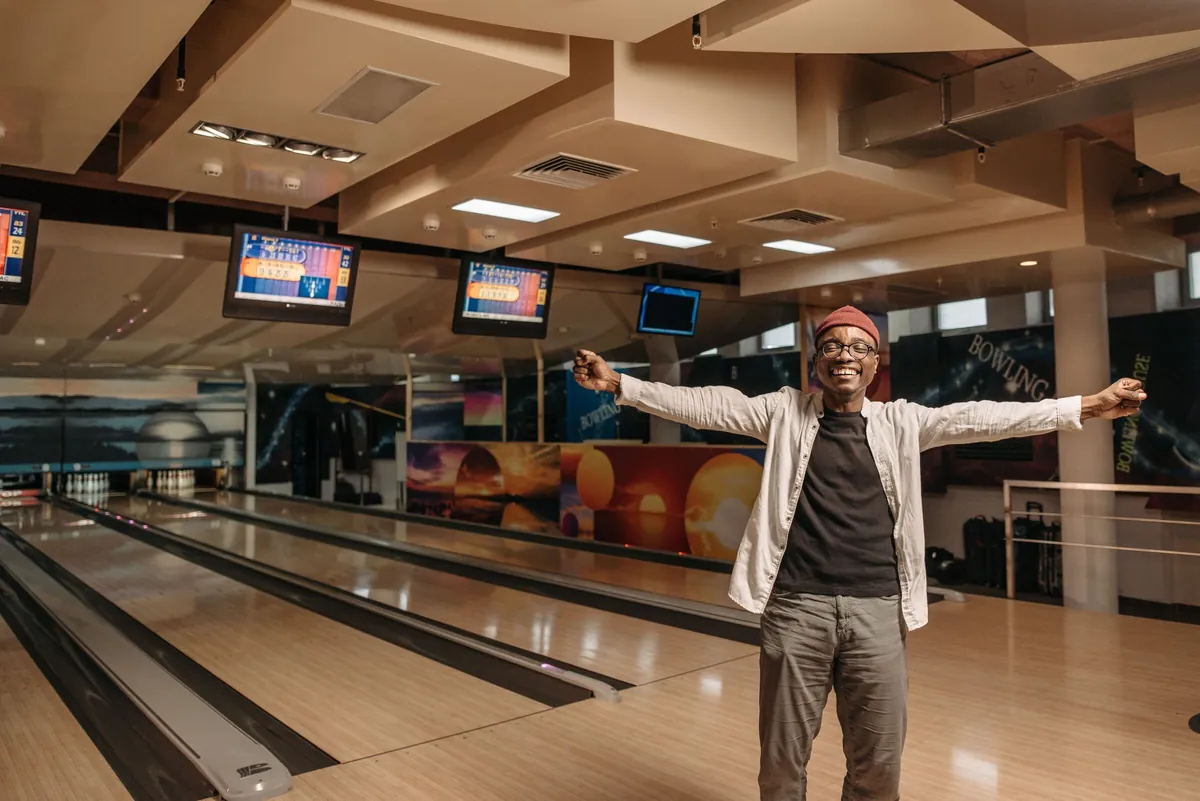 Smiling man with arms wide open, enjoying a relaxed moment on a bowling lane