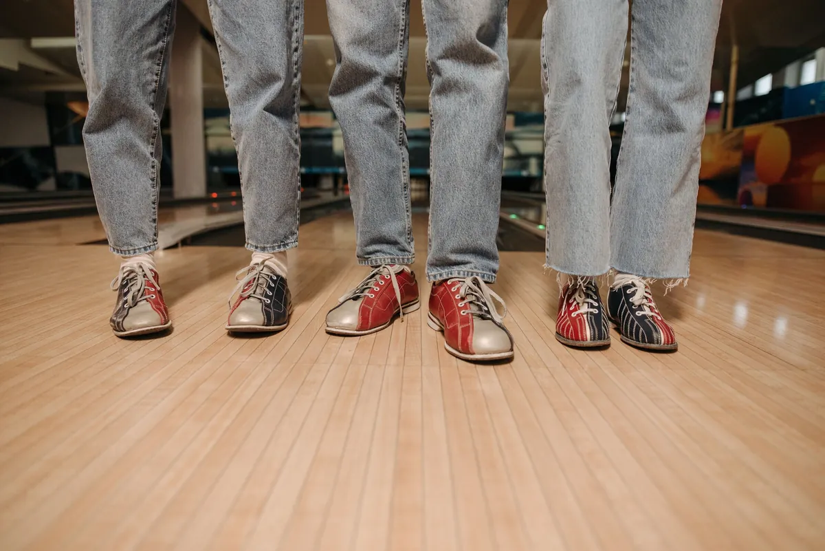 Three pairs of colourful bowling shoes worn by players on the wooden floor of the lane