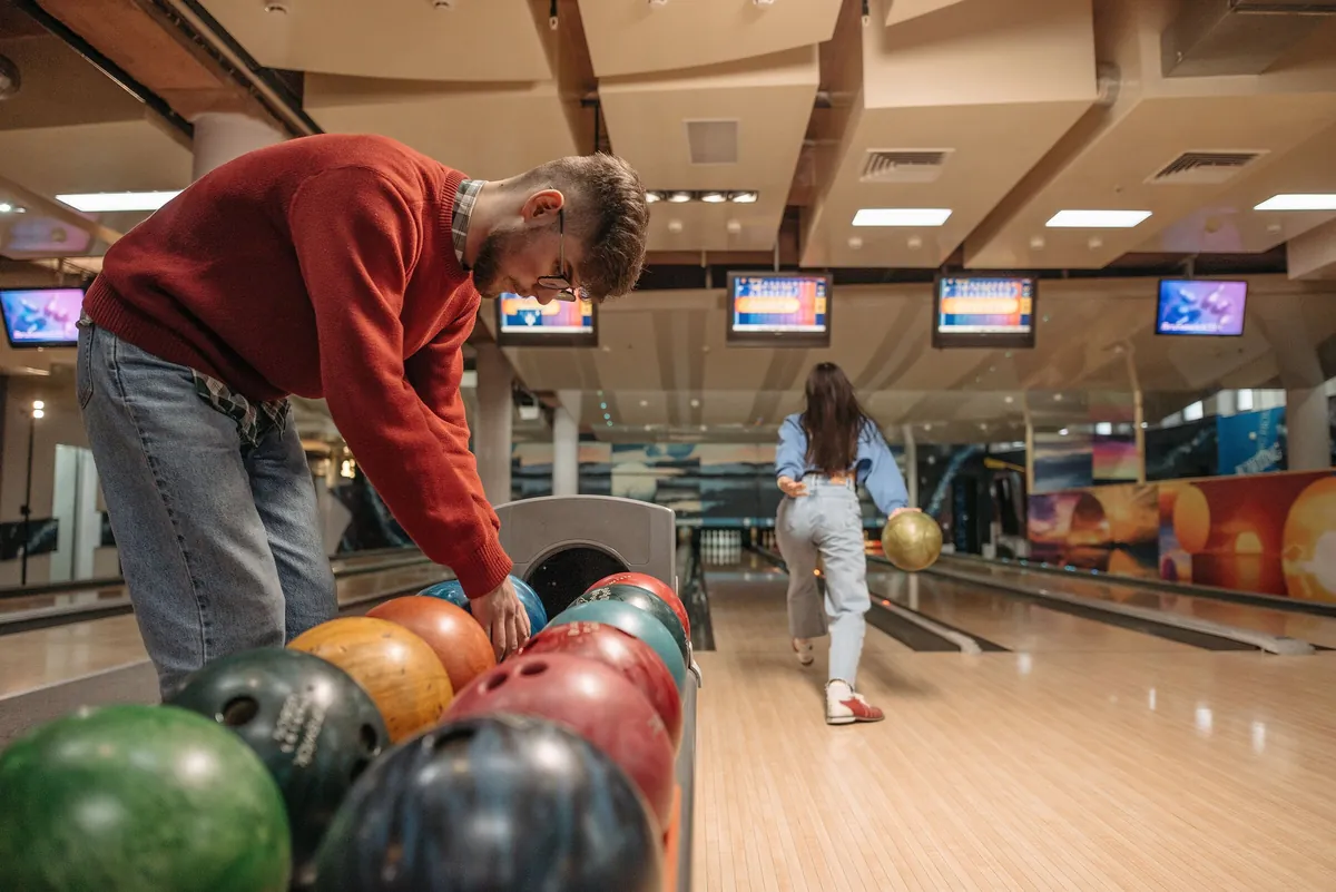 Bowler choosing a bowling ball from a rack of colourful balls, with lanes in the background