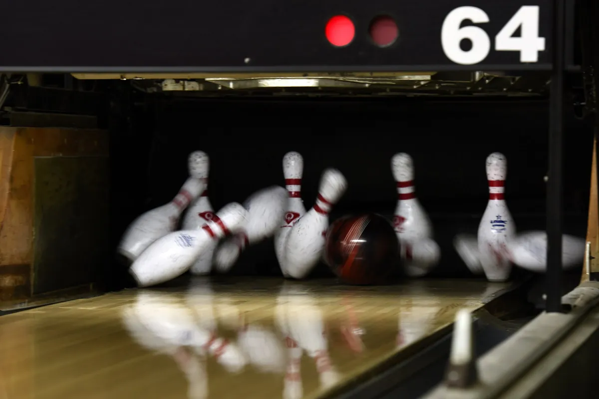 A bowling ball smashing into the pins as they fly in all directions during a strike on the lane