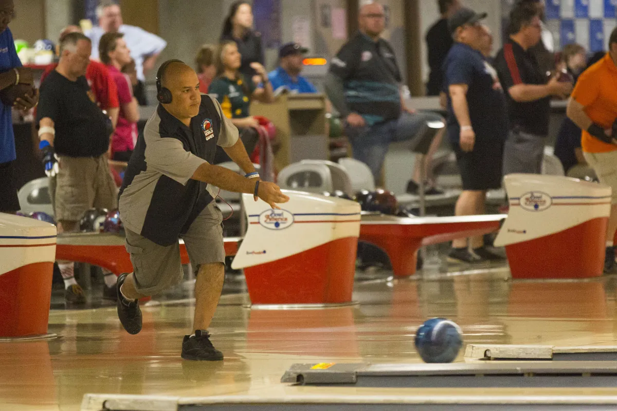 Bowler mid-delivery during a bowling tournament, with competitors and spectators in the background