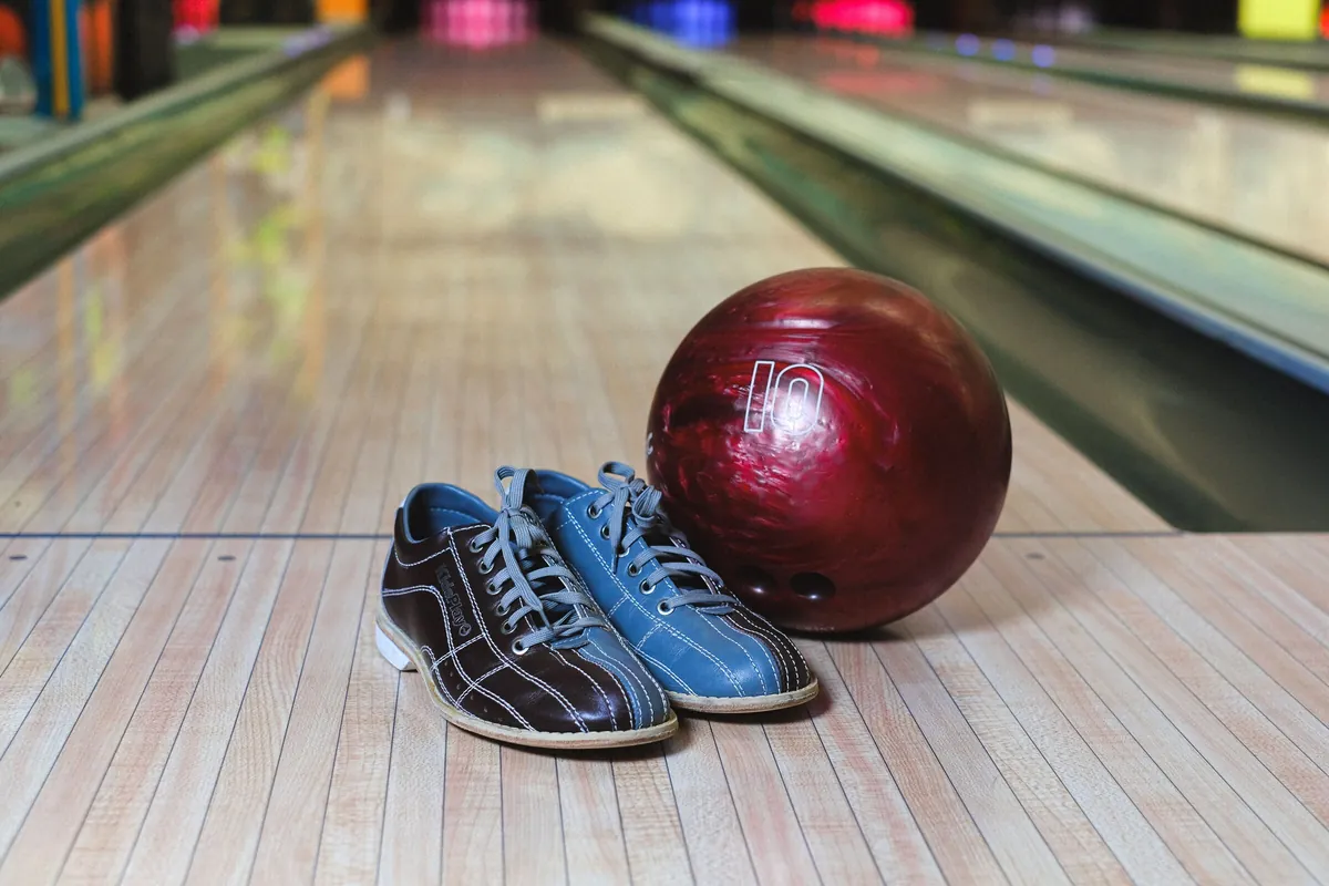 Bowling shoes and a burgundy ball resting on the varnished wood of a bowling lane