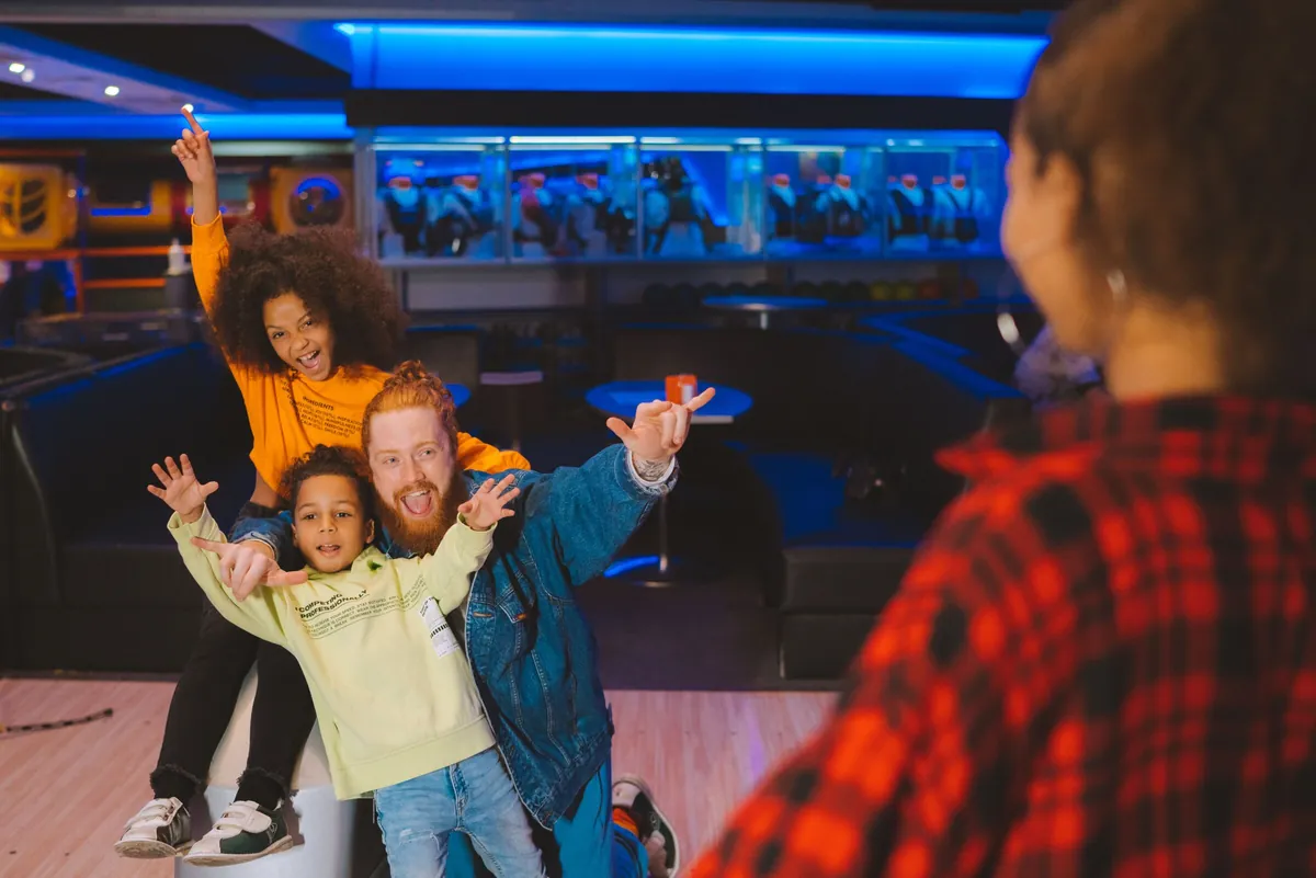 Enfants et parent levant les bras de joie lors d'un anniversaire au bowling