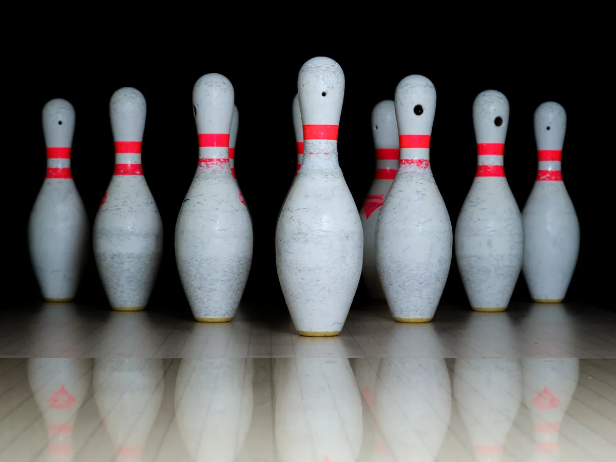 A row of white bowling pins with red stripes reflected on a dark lane