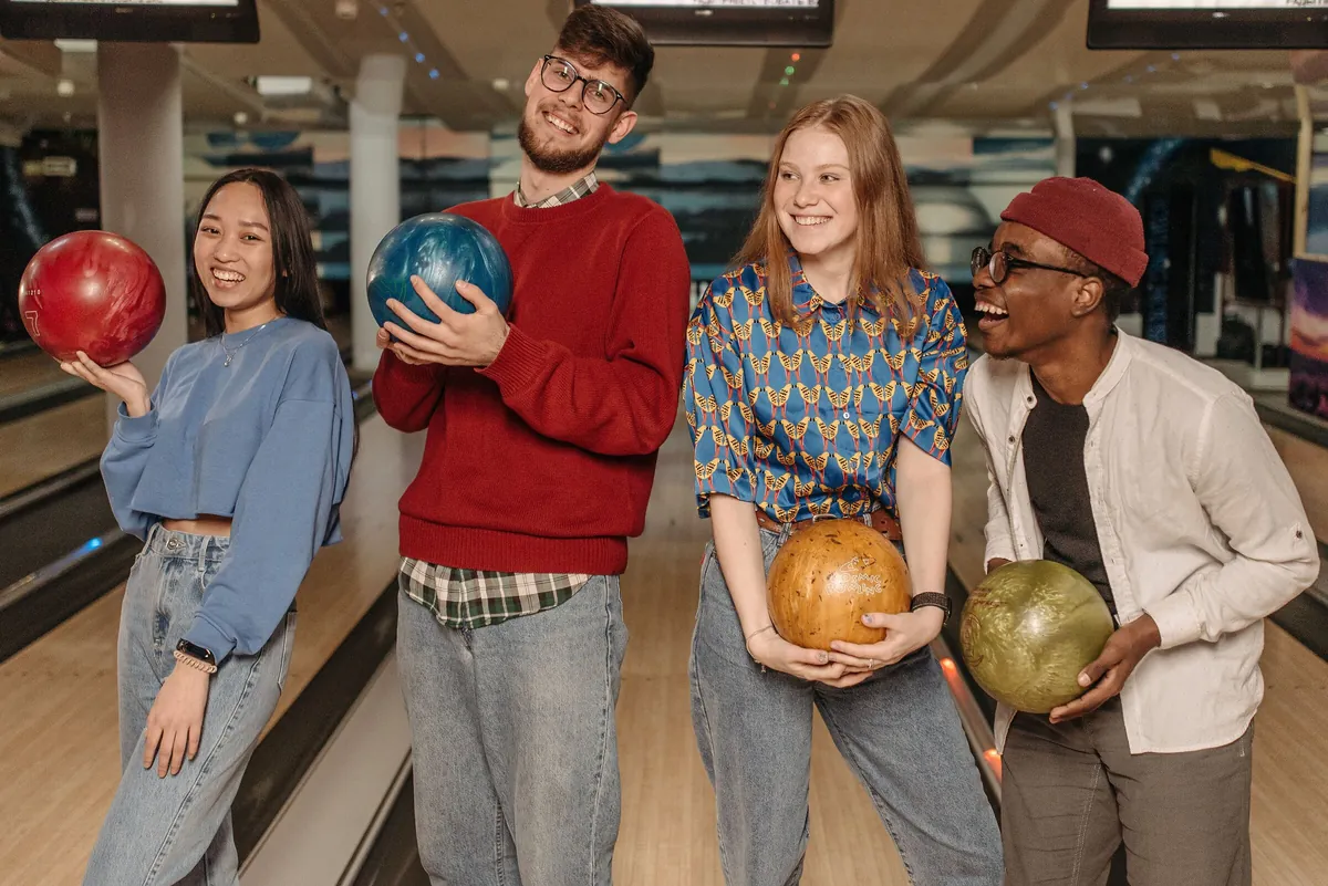 Four smiling friends holding colourful bowling balls before starting their game